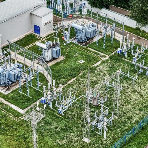 Aerial view of the city electrical substation standing on a green lawn and surrounded by dense greenery