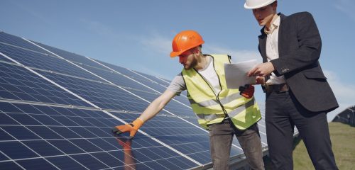 Businessman and worker near solar energy batteries. Business client showing photovoltaic detail to foreman. Two men making deal.