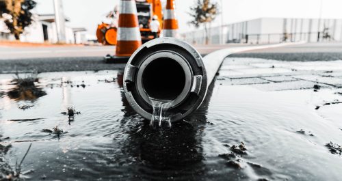 A selective closeup shot of a gray pipe with water coming out its hole