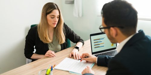 Professional lawyer explaining and reviewing a business contract with a female client at the office. Caucasian woman listening to her male boss talk about a work report
