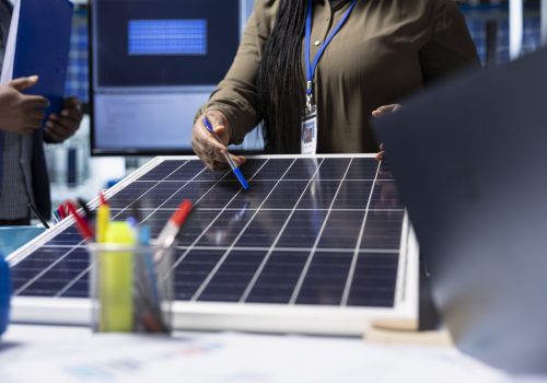 Shareholders meet with industrial plant manager to review solar panel components, analyzing material quality. Photovoltaics factory management executive presents solar panel features to investors