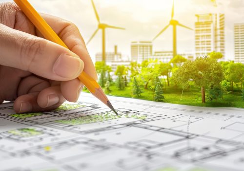 A detailed view of a sustainable city planning process with a hand placing miniature green trees and structures.