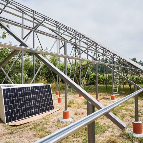 Worker installing solar panel on metal beams in field at daytime. Renewable and ecological energy. Photo-voltaic collection of modules as a PV panel. Array as a system of photo-voltaic panels.